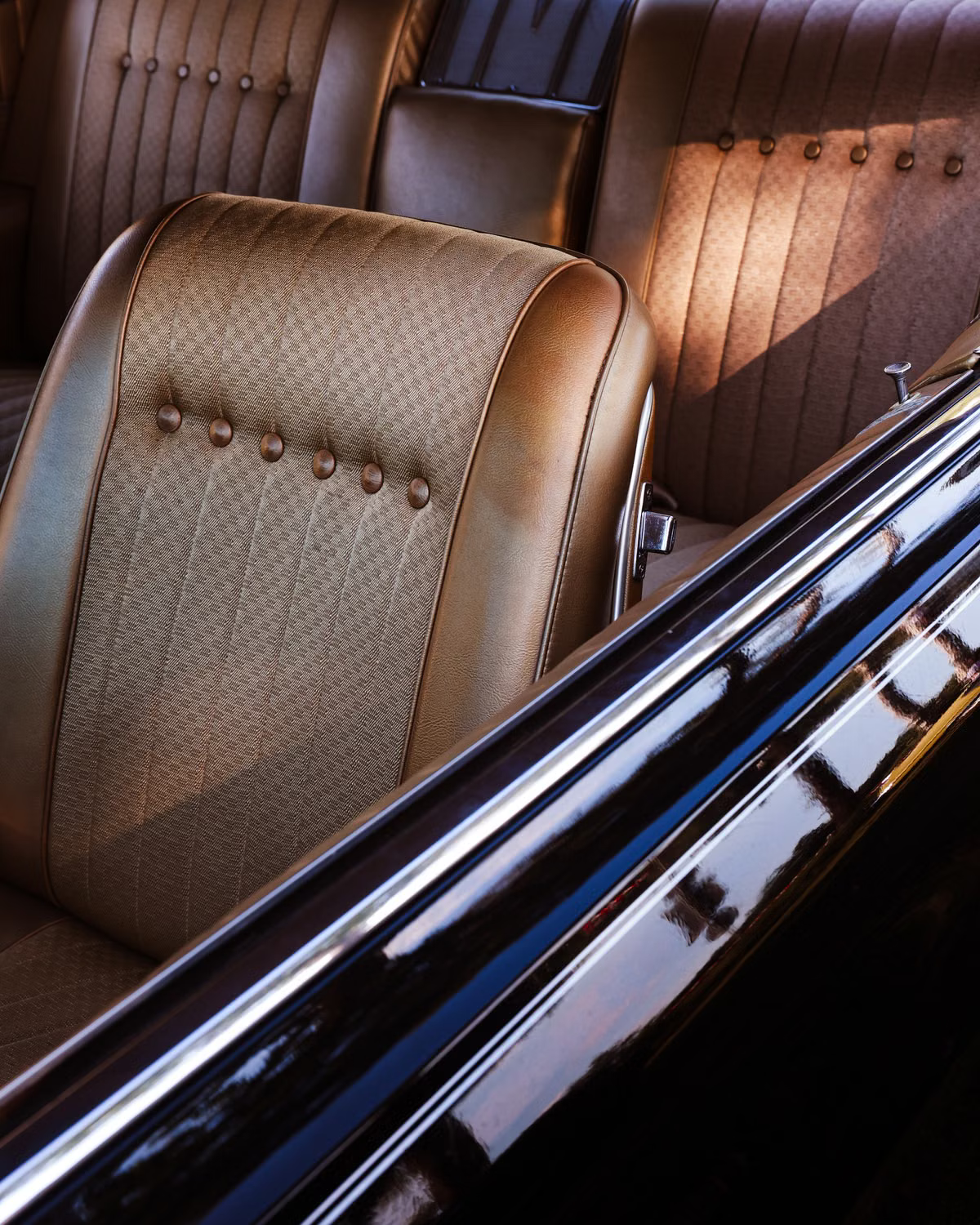 Bronze tufted seat of a classic car seen through the open window frame