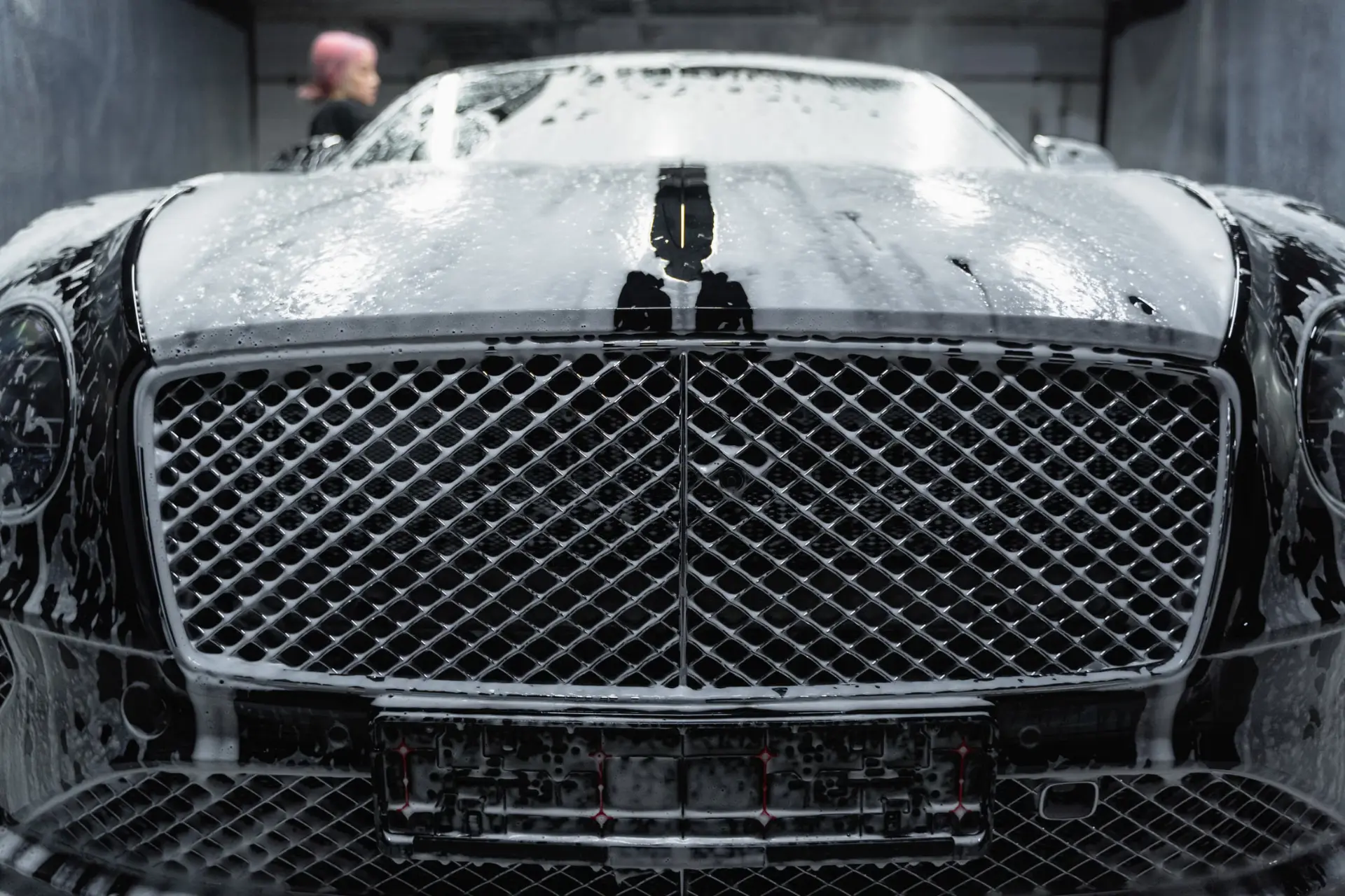 Foam-covered luxury car being hand washed in a detailing bay